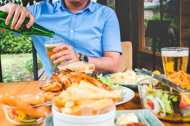 Trinkendes Bier des jungen asiatischen Mannes und eatting Nahrungsmittel glücklich beim nach Hause genießen