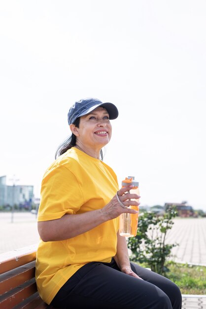 Trinkendes Trinkwasser der älteren Frau nach dem Training im Freien auf dem Sportplatz
