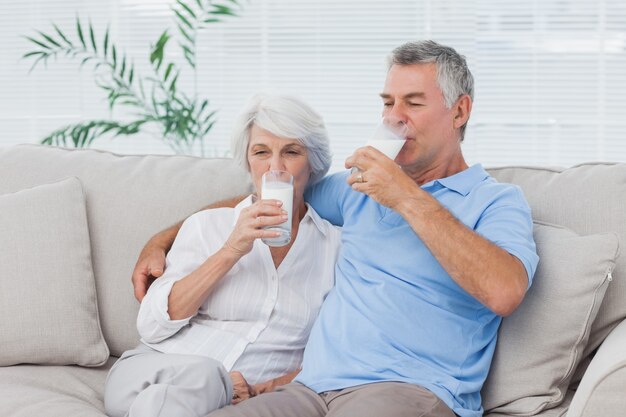 Trinkgläser der Paare Milch sitzend auf der Couch