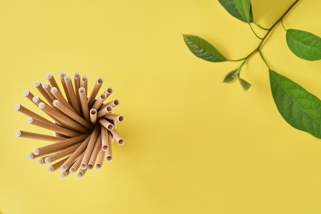 Trinkröhrchen aus Papier und Maisstärke, biologisch abbaubarem Material und Öko-Papiergläsern mit grünen Sprossenblättern auf gelbem Trendfarbenhintergrund 2021. Null Abfall und plastikfreies Konzept. Draufsicht