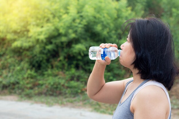 Trinkwasser der Asiatin nach Sportübung, Sportfrau, die Flasche reines Wasser hält