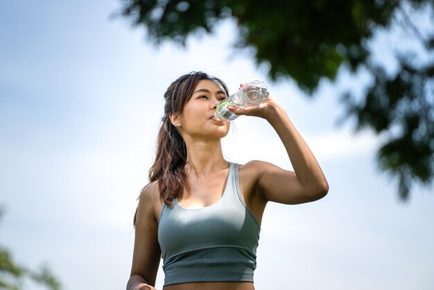 Trinkwasser der Eignungsfrau Junge durstige Frau trinkt Wasser aus einer Flasche im Sommerpark Sport