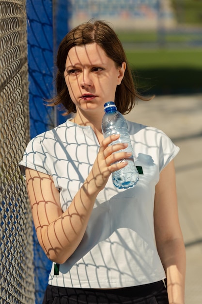 Trinkwasser der Frau nach dem Fitnesstraining auf dem Sportplatz im Freien