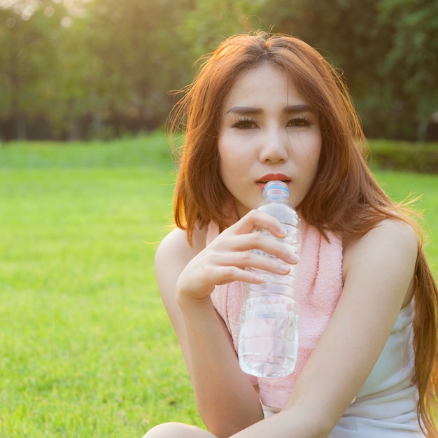 Trinkwasser der Frau und sitzen auf Gras.