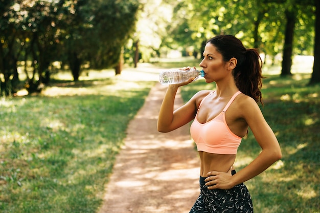 Trinkwasser der Ftness-Athletenfrau nach arbeiten das Trainieren im Freien aus.