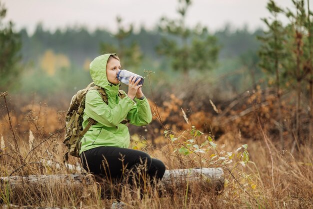 Trinkwasser der jungen Frau mit Rucksack am Waldtal