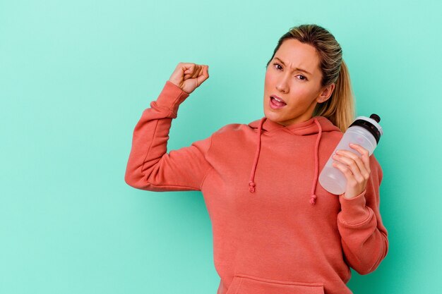 Trinkwasser der jungen Sportfrau lokalisiert auf blauer wallraising Faust nach einem Sieg