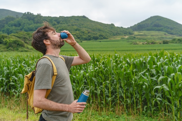 Trinkwasser des abenteuerlustigen Mannes unterwegs. Horizontale Ansicht des Mannes, der auf Kornfeld mit Süßwasser wandert.