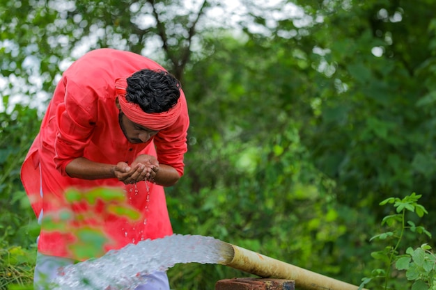 Trinkwasser des indischen Bauern mit der Hand von der Pipeline am Feld