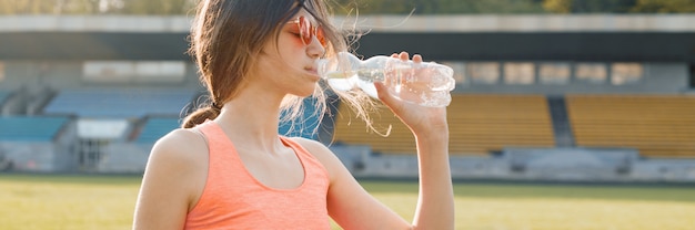 Trinkwasser des Jugendlichen des jungen Mädchens von der Flasche nachdem dem Laufen