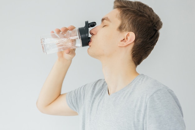 Trinkwasser des jungen Mannes im grauen Hemd während des Sports. Sport zu Hause. Mann auf grauem Hintergrund