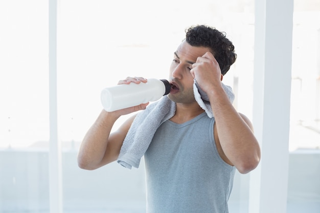 Trinkwasser des Mannes beim Abwischen schwitzt mit Tuch im Eignungsstudio