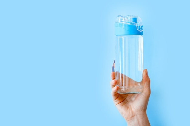 Trinkwasserflasche für Sport in weiblicher Hand auf blauem Hintergrund mit Kopienraum. Wiederverwendbare Flasche. Gesunder Lebensstil und Fitnesskonzept.