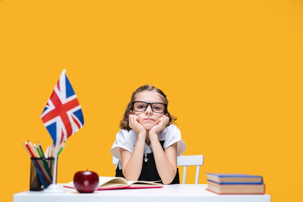 Triste y aburrida colegiala caucásica en gafas estudiando en casa lección de inglés bandera de gran bretaña