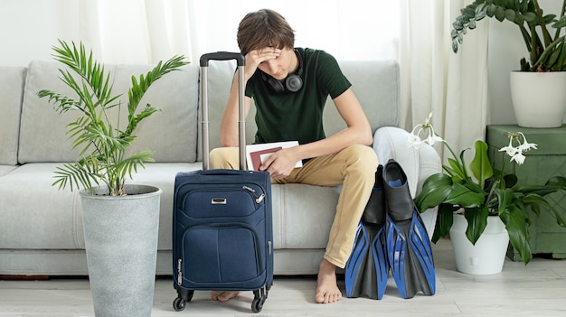 Triste adolescente turista con una maleta y aletas se queda en casa