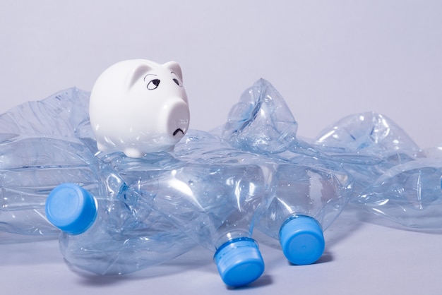 Foto triste alcancía y un montón de botellas de plástico arrugadas desechables