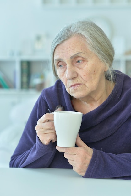 Triste anciana con dolor de cabeza bebiendo té
