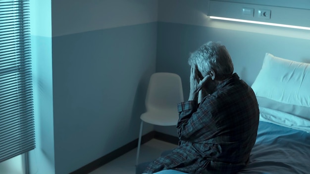 Triste anciano solitario sentado en una cama de hospital por la noche