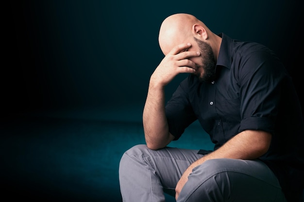 Triste y apuesto joven sentado y apoyando la cabeza con la mano