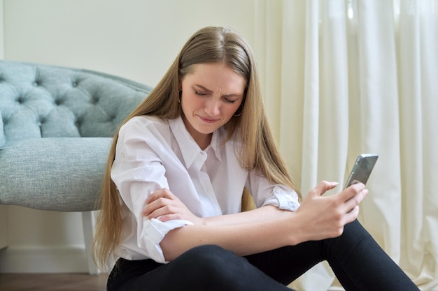 Triste chorando jovem com smartphone sentado no chão em casa