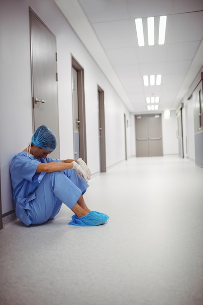 Triste cirujano sentado en el piso en corredor