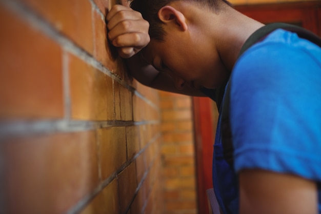 Triste colegial apoyado en la pared de ladrillo