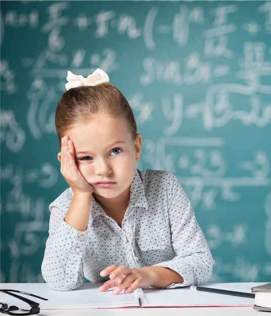 Triste colegiala con libro sobre fondo de pizarra