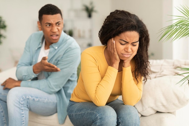 Triste e chorosa jovem afro-americana ignora um cara bravo e agressivo sentado no sofá