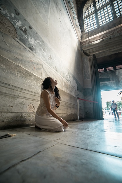 Triste e perdida a esperança, a menina reza no templo ajoelhada sob os raios da luz divina.