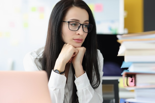 Triste empresaria mira gran pila de carpetas con documentos en el lugar de trabajo. Burnout en el concepto de trabajo