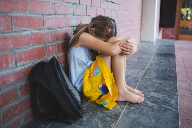 Triste escolar sentado solo en el pasillo