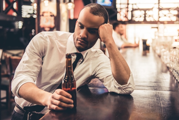 Triste guapo empresario afroamericano está bebiendo cerveza.