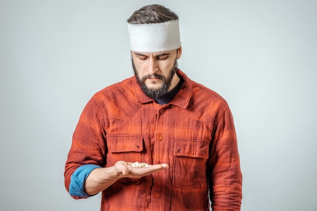 Foto triste herido hombre vendado con pastillas sobre fondo gris