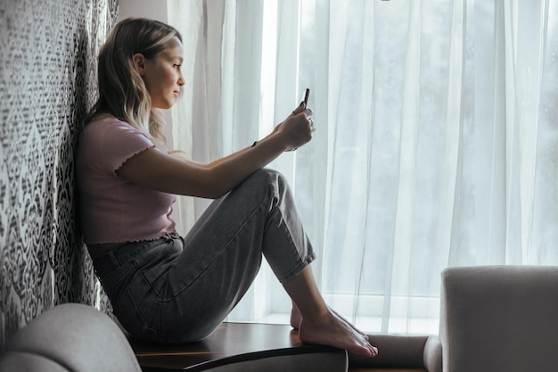 Triste hermosa chica mirando el teléfono en casa