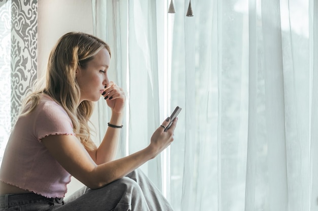 Triste hermosa chica mirando el teléfono en casa