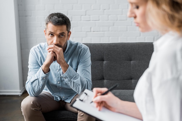Triste hombre adulto en sesión de terapia de psicólogo en la oficina