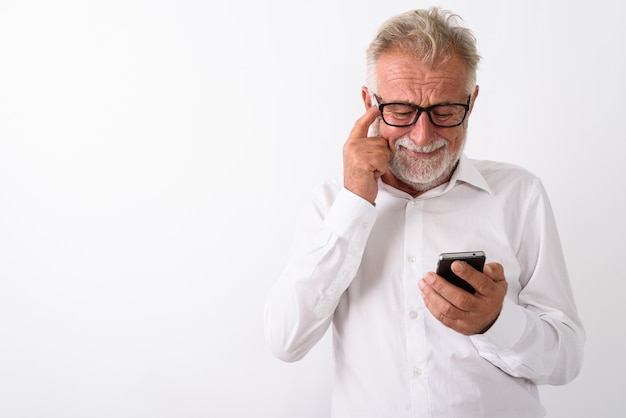 Triste hombre barbudo senior mediante teléfono móvil mientras se rasca la cabeza con anteojos en blanco