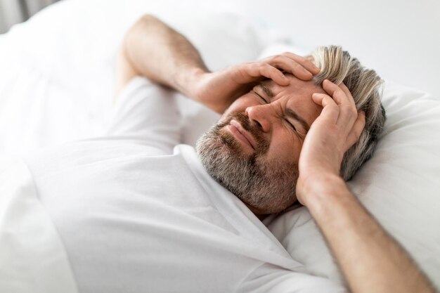 Triste hombre de mediana edad acostado en la cama tocando la cabeza