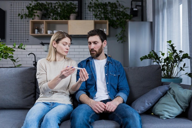 Triste homem e mulher sentados no sofá decepcionados com um teste de gravidez negativo