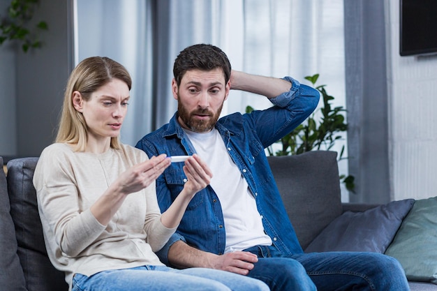 Triste homem e mulher sentados no sofá decepcionados com um teste de gravidez negativo