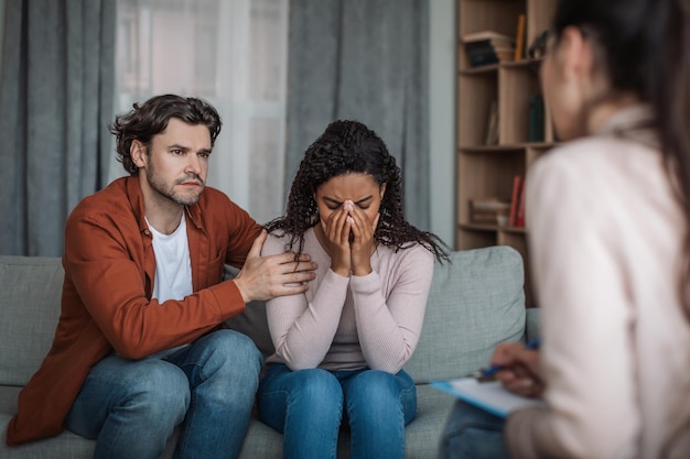 Triste homem europeu do milênio confortando uma mulher afro-americana chorando em consulta com