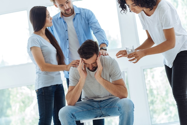 Foto triste infeliz hombre barbudo sosteniendo sus sienes e inclinándose hacia adelante mientras sufre de migraña