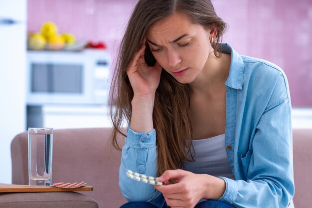 Triste infeliz mulher estressada tomando pílulas de analgésicos de forte dor de cabeça em casa. Sentindo enxaqueca e fadiga física