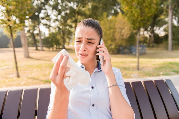 Triste jovem chora enquanto fala ao telefone móvel ao ar livre