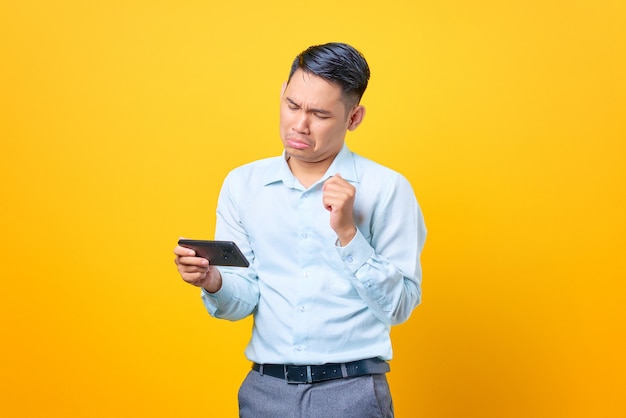 Triste jovem e bonito empresário jogando um jogo no celular em fundo amarelo