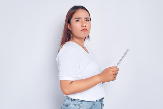 Triste joven asiática en camiseta blanca sosteniendo tableta digital aislada en el concepto de personas de estilo de vida de fondo blanco