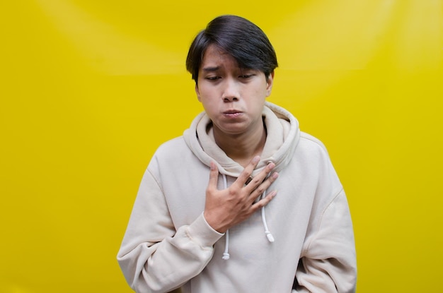 Triste Un joven asiático con una camiseta gris con una expresión de cara de llanto está aislado en amarillo