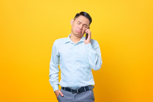 Triste joven empresario guapo hablando por un teléfono inteligente sobre fondo amarillo