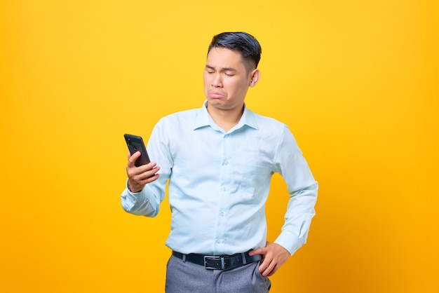 Triste joven empresario guapo mirando la pantalla del teléfono móvil sobre fondo amarillo