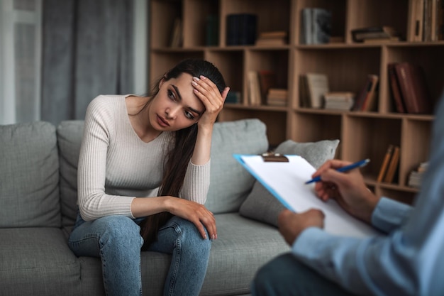 Triste joven europea sostenga su cabeza con la mano en consulta con un médico psicólogo con